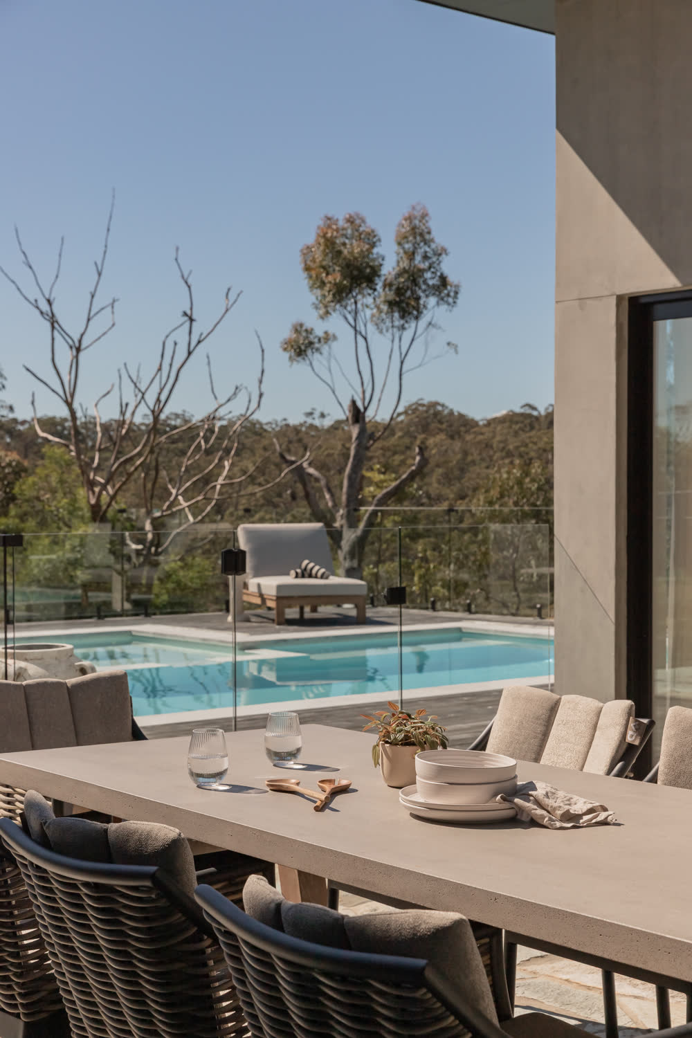 Outdoor dining terrace at Glenorie — table set on crazy-paved flagstone under the roofline, pool and glass fence beyond
