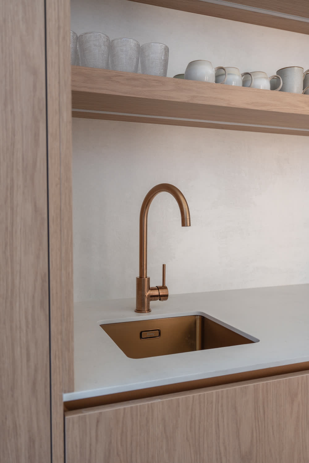 Butler's pantry at Glenorie — brass sink and gooseneck mixer in a stone benchtop, timber shelving above with glassware and crockery