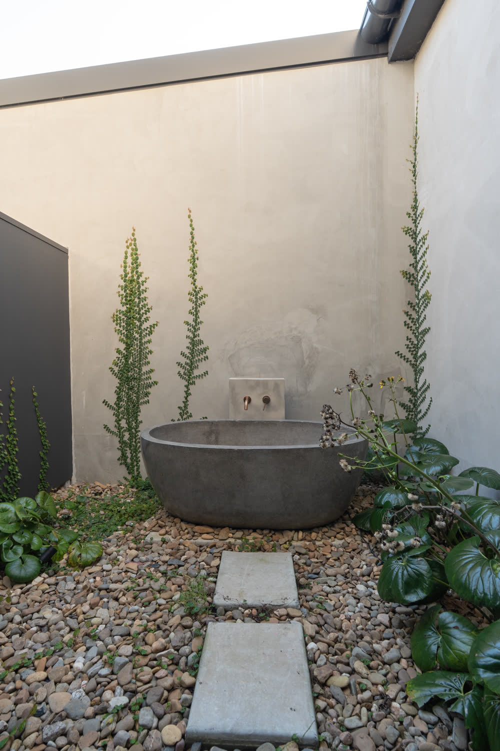 Carved stone outdoor tub set among river pebbles and espaliered plants in the private bathing courtyard at Glenorie