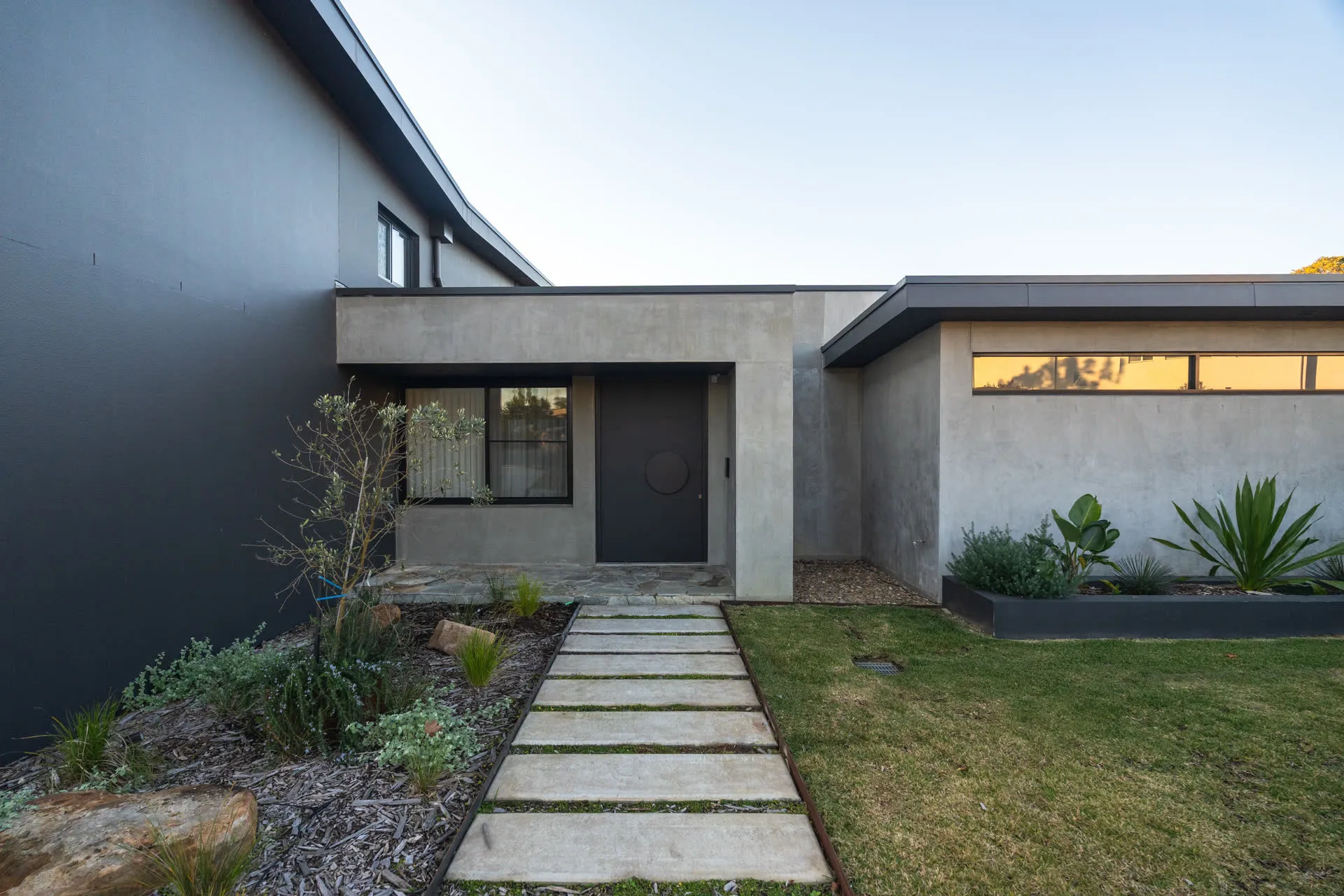 The Glenorie house at dusk — dark cladding and concrete against the last light, garden path lit