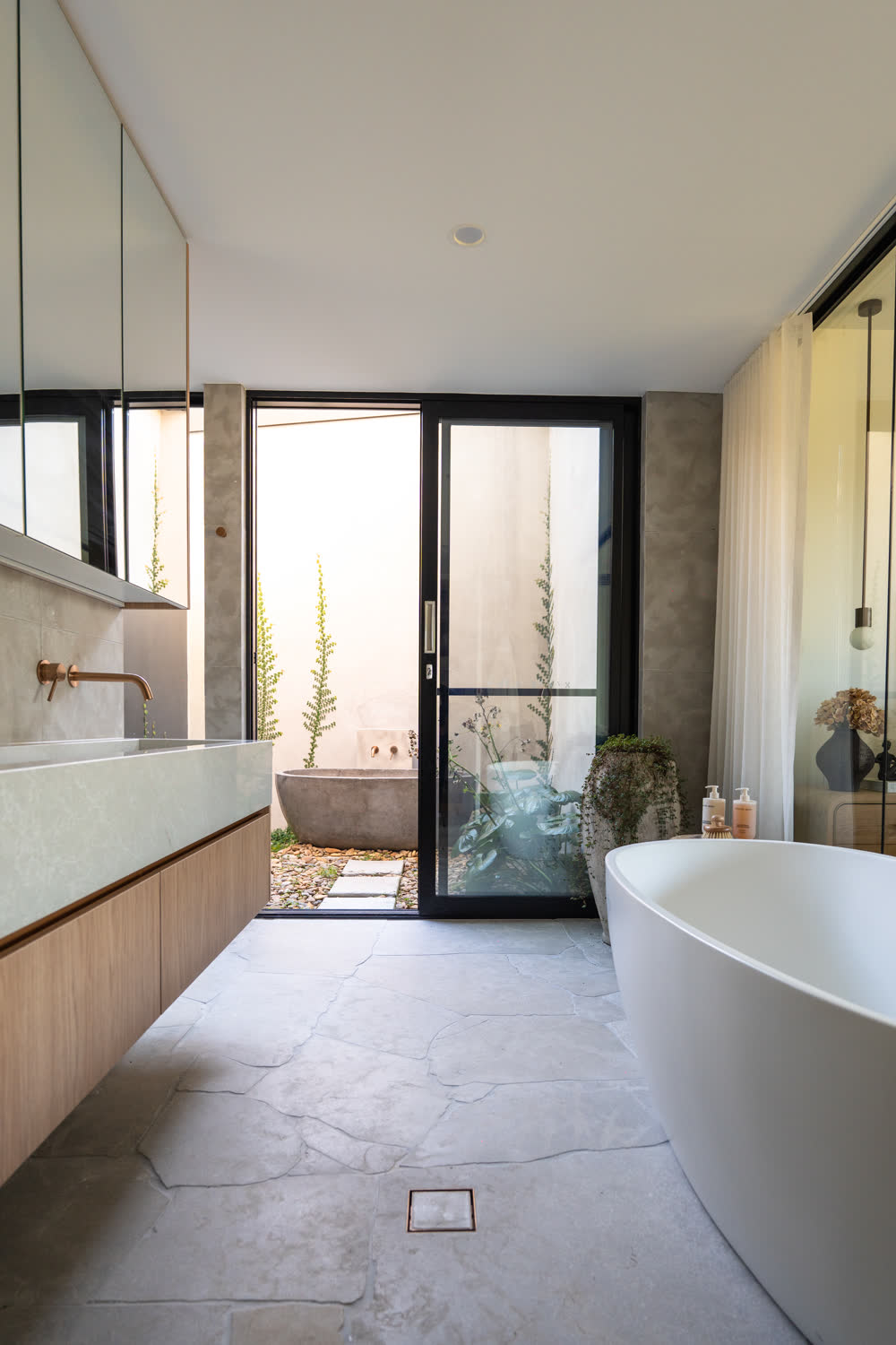 Freestanding bath with floor-mounted brass filler in the Glenorie ensuite, glazing to the bathing courtyard beyond