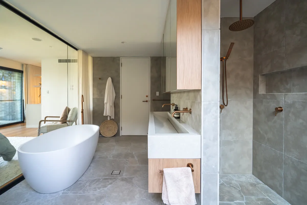The full ensuite at Glenorie — freestanding bath, stone trough vanity and shower, with the bedroom beyond the glass