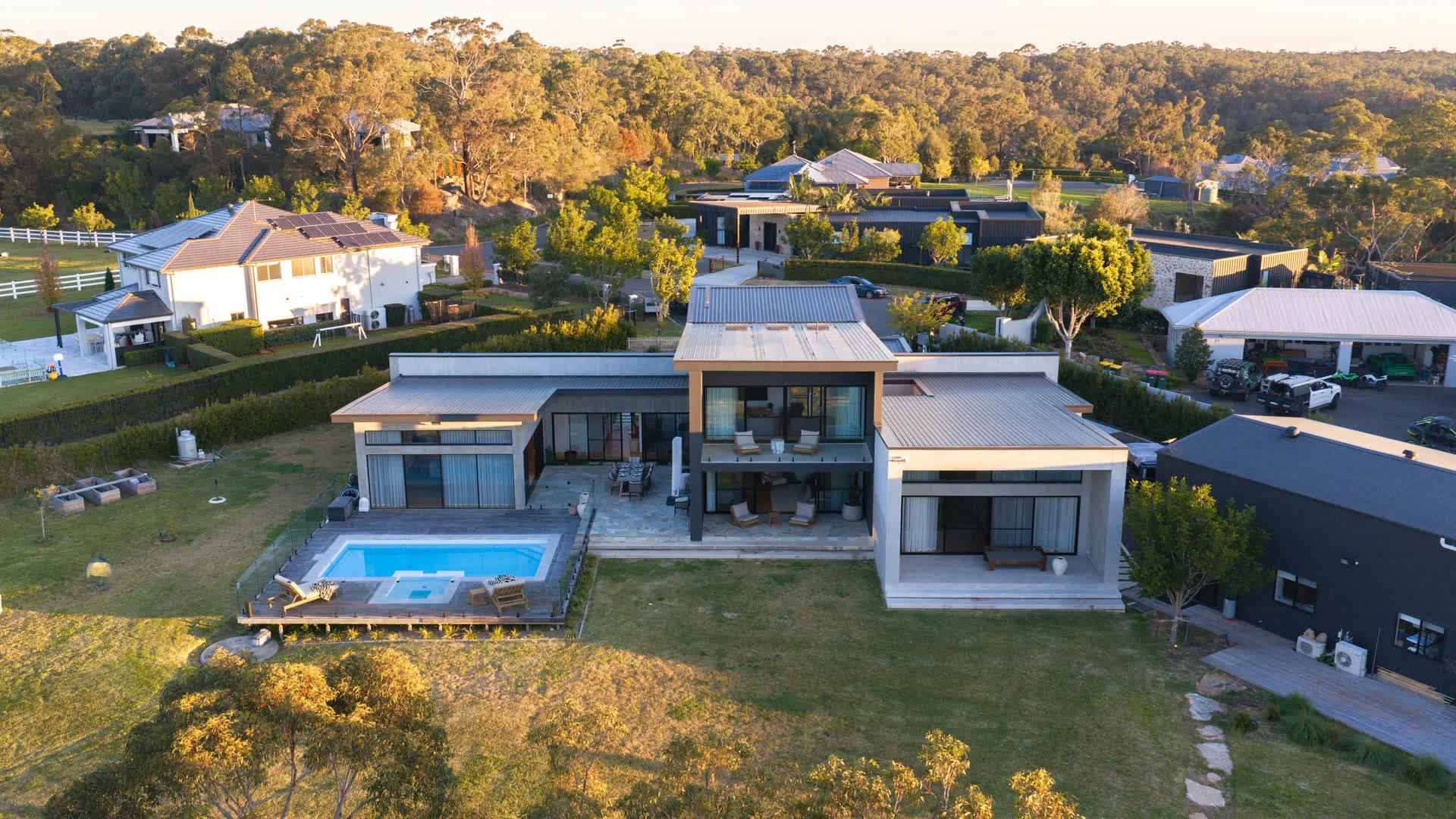 Drone photograph of the completed Glenorie property at golden hour — both dwellings, the pool and the bushland edge of the estate