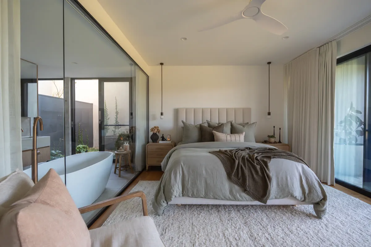 The master suite at Glenorie — bed dressed in linen, the freestanding bath visible behind a glass wall to the courtyard