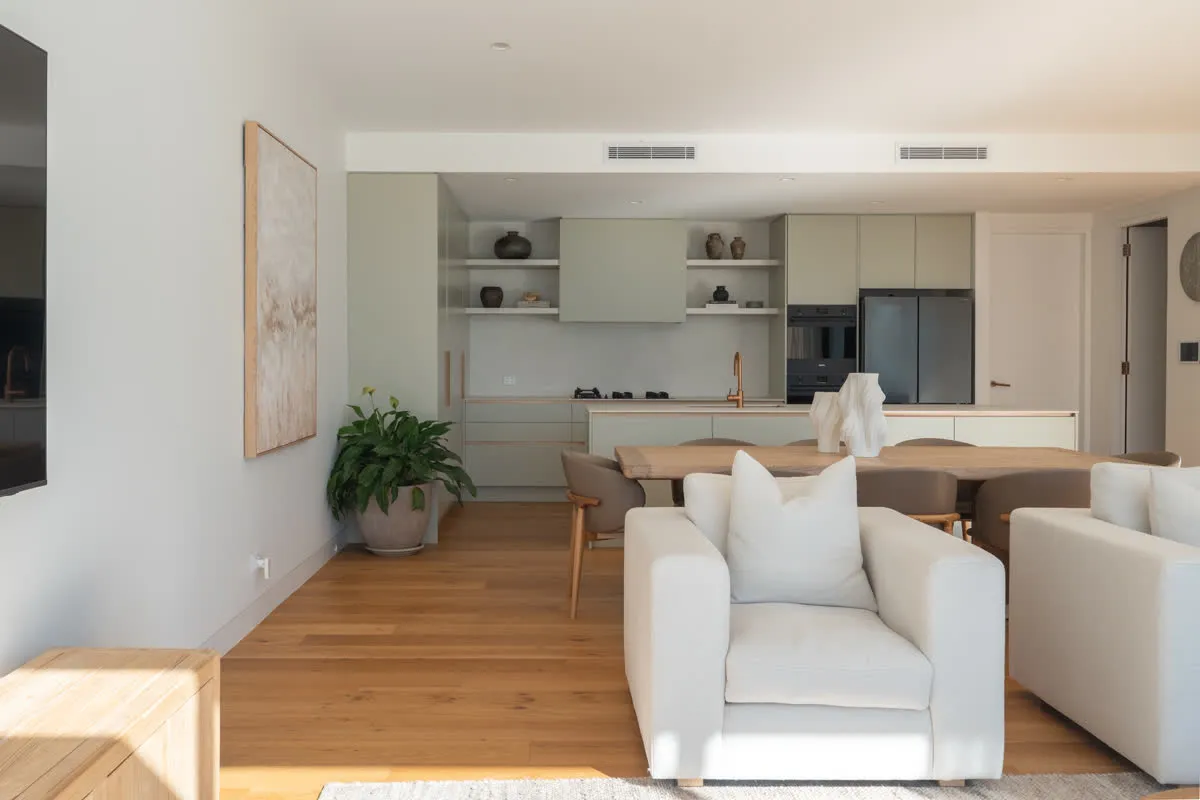 Open-plan living at Glenorie — sage kitchen and island beyond the dining table and lounge