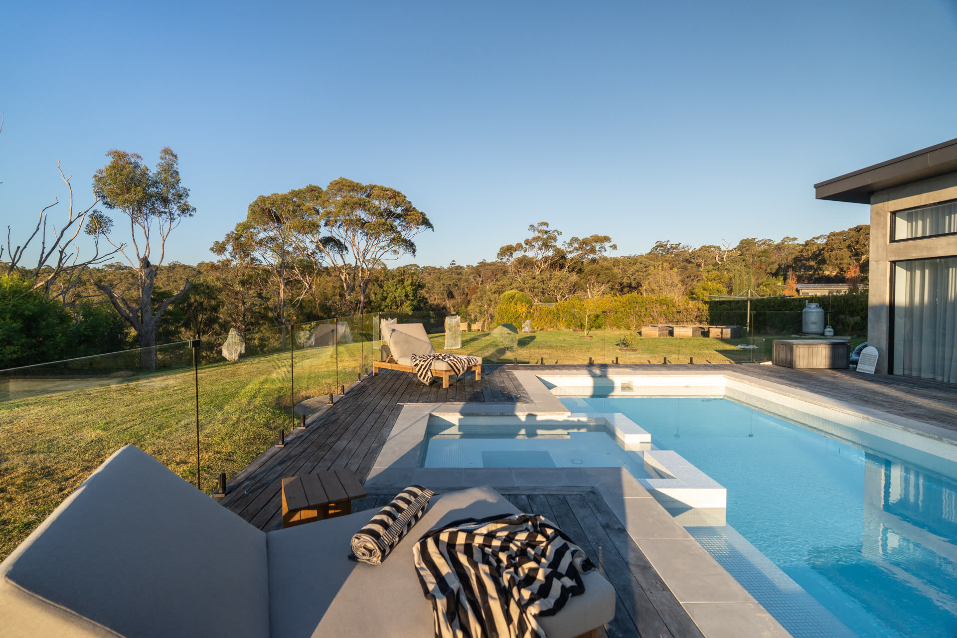 The Glenorie pool and spa at dusk, lounges on the timber deck and the bushland ridge behind
